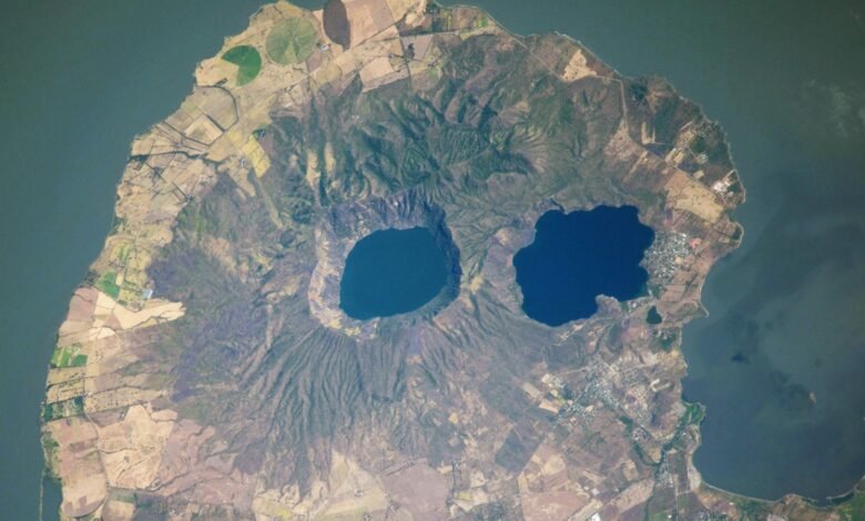 تحدق "العيون البركانية" البركانية في الفضاء من شبه جزيرة تشبه الجمجمة - الأرض من الفضاء 1 A satellite photo of a rounded peninsula in a lake, with two eye-like lakes at its center