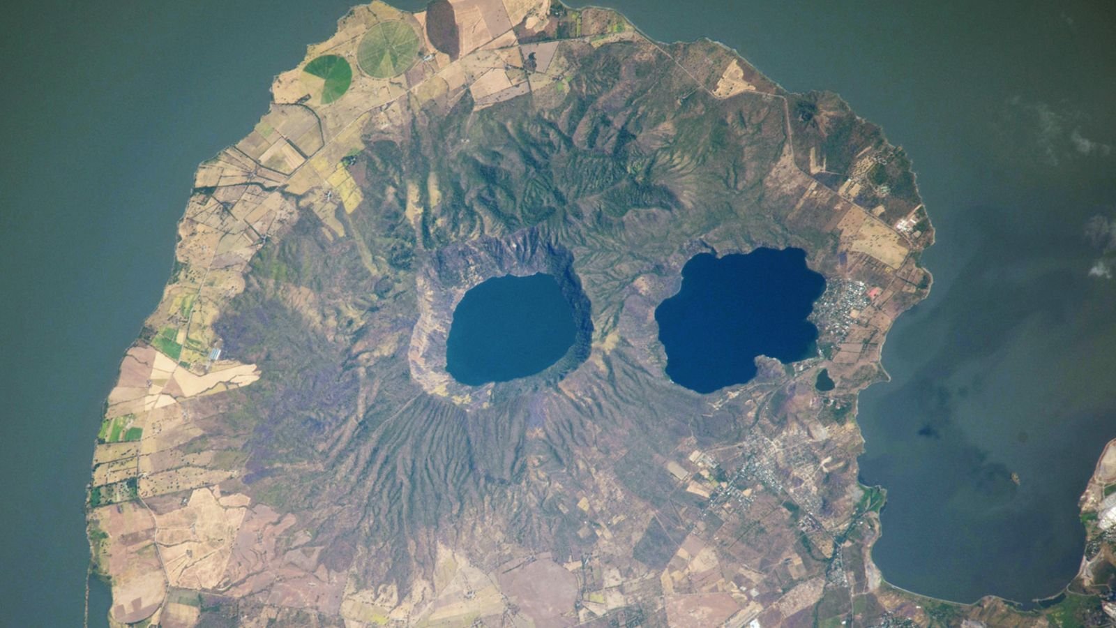 تحدق "العيون البركانية" البركانية في الفضاء من شبه جزيرة تشبه الجمجمة - الأرض من الفضاء 3 A satellite photo of a rounded peninsula in a lake, with two eye-like lakes at its center